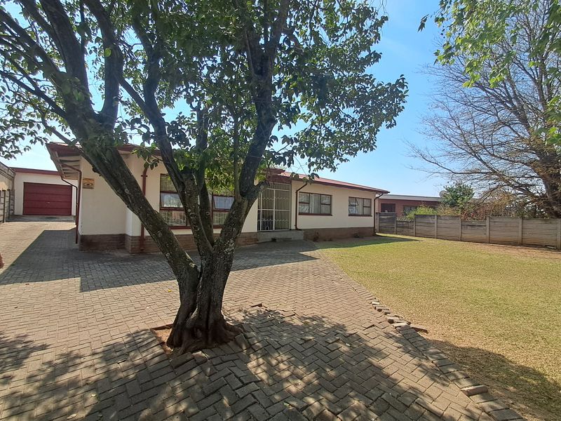 Rear view of the property featuring a paved driveway, a spacious lawn, and a secure perimeter wall.
