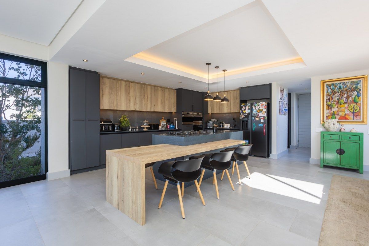 Modern kitchen featuring dark cabinetry, wood-tone accents, a central island with integrated seating, and recessed ceiling lighting with cove detail.