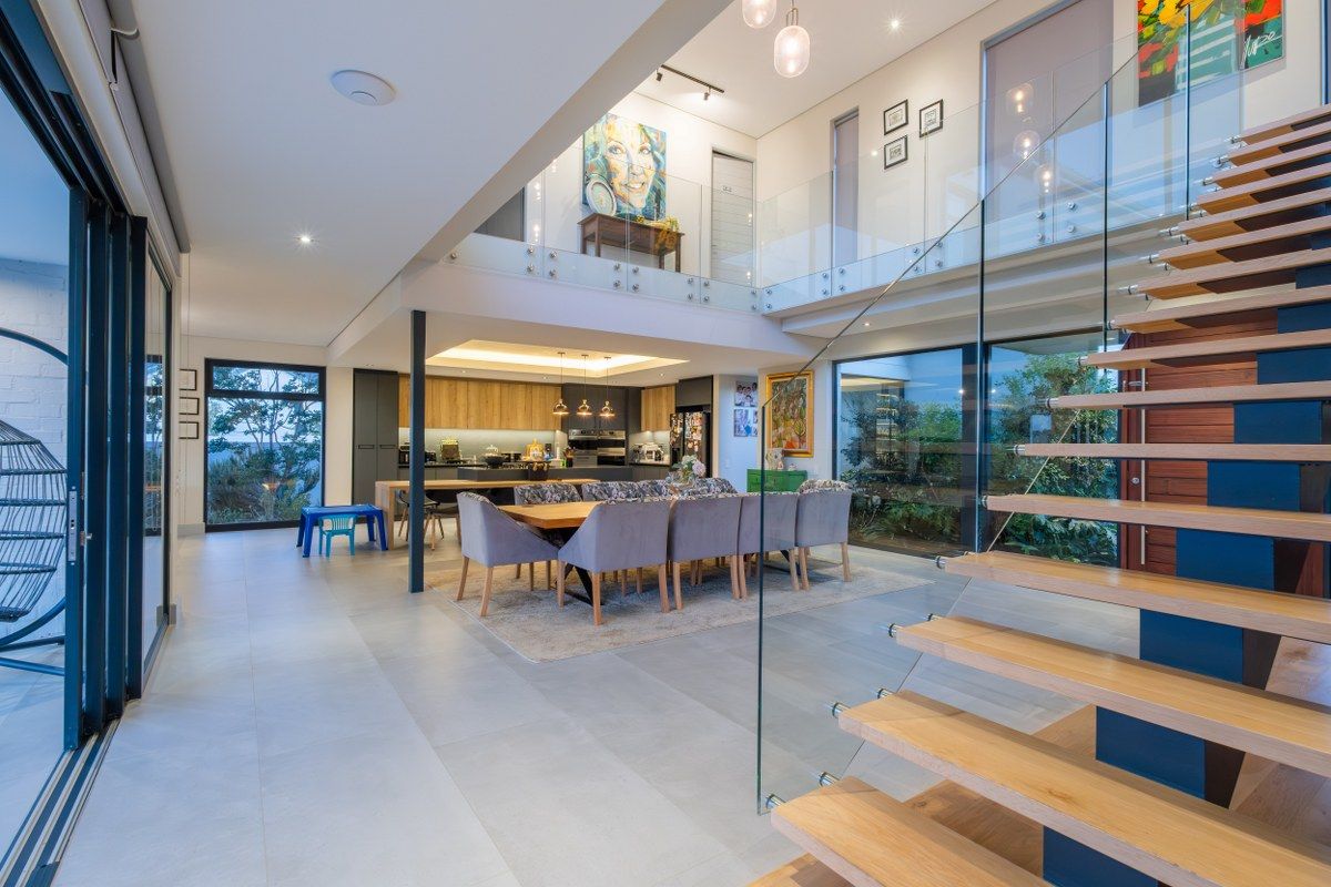 Spacious open-plan living and dining area featuring a modern floating staircase, glass balustrades, and seamless integration with the kitchen and outdoor spaces.