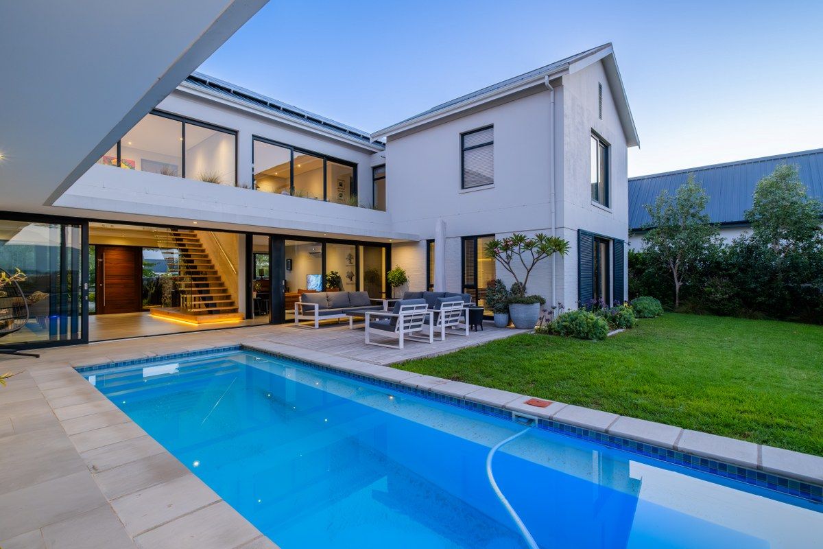 Modern rear exterior featuring a swimming pool, timber deck, landscaped garden, and seamless indoor-outdoor flow through large sliding glass doors.