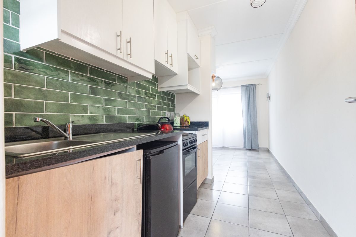 Modern galley-style kitchen featuring green subway tile backsplash, granite countertops, light wood cabinetry, and ceramic floor tiles.