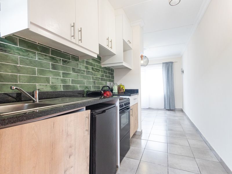 Modern galley-style kitchen featuring green subway tile backsplash, granite countertops, light wood cabinetry, and ceramic floor tiles.