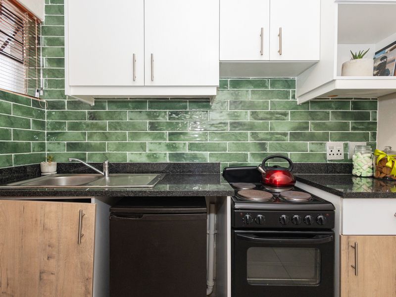 Compact kitchen featuring green subway tile backsplash, granite countertops, stainless steel sink, and built-in cabinetry with an integrated electric stove and oven.
