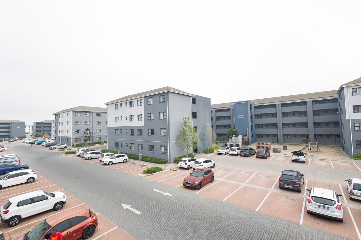 An aerial view of a modern apartment complex featuring multi-story residential blocks, paved parking bays, and communal outdoor spaces.