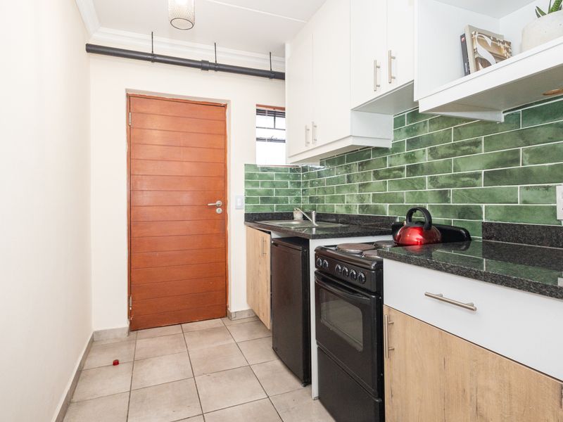 A compact kitchen featuring modern green subway tile backsplash, granite countertops, built-in cabinetry, and a freestanding stove.