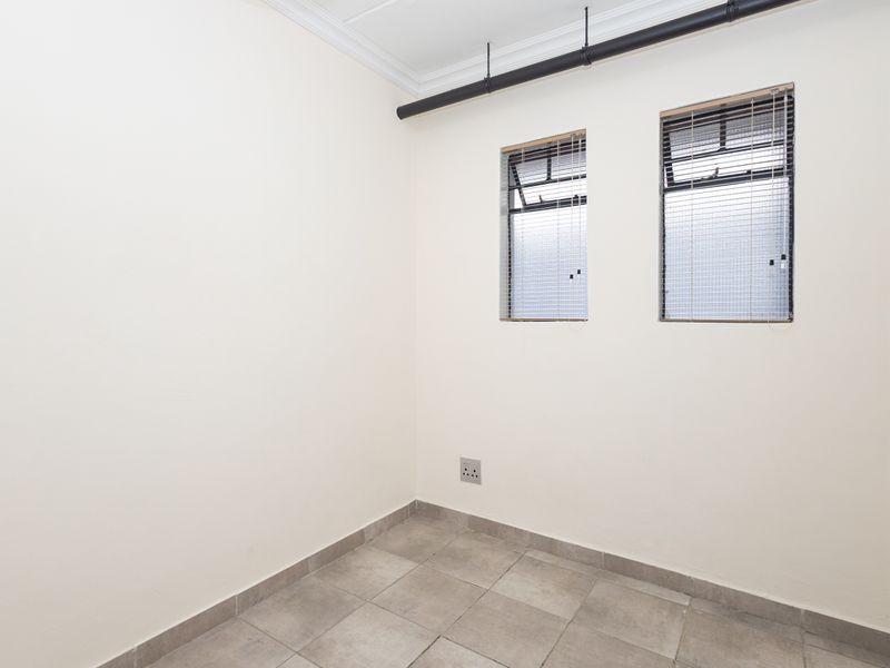 A clean, empty bedroom featuring tiled flooring, neutral walls, and functional venetian blinds, providing a versatile space ready for personalization.