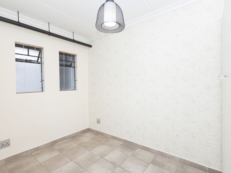 A bright, empty bedroom featuring tiled flooring, patterned wallpaper, and industrial-style exposed pipework, offering a clean and neutral space ready for furnishing.