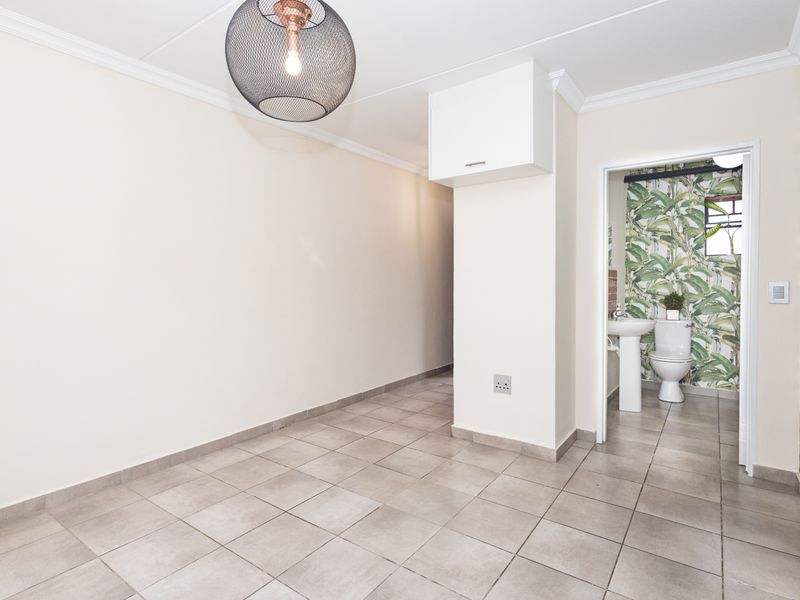 A clean, tiled hallway area leading into a bathroom featuring a pedestal basin and toilet with decorative wallpaper.