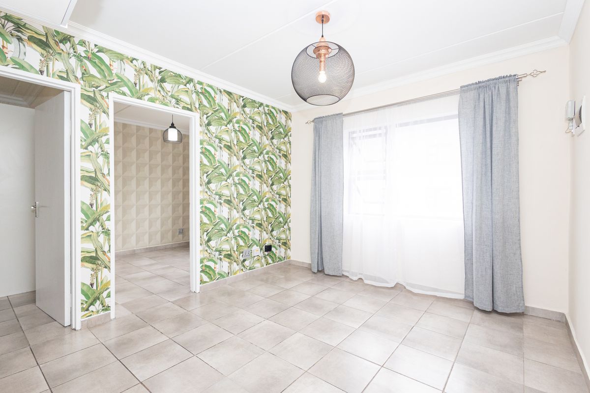 A bright, empty living area featuring neutral tiled flooring, decorative botanical wallpaper, and crown molding, with a view into an adjacent room.