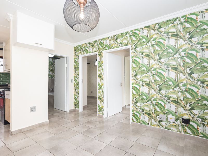 Open plan living area featuring tiled floors, a compact kitchen with built-in cabinetry, and decorative wallpaper leading to adjacent rooms.