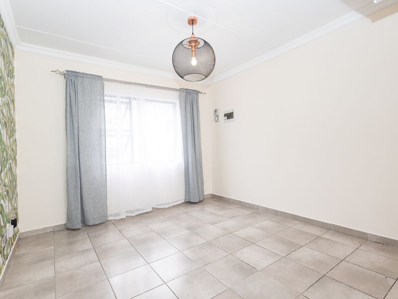 A bright, empty bedroom featuring neutral tiled flooring, a decorative feature wall, and a modern pendant light fixture.