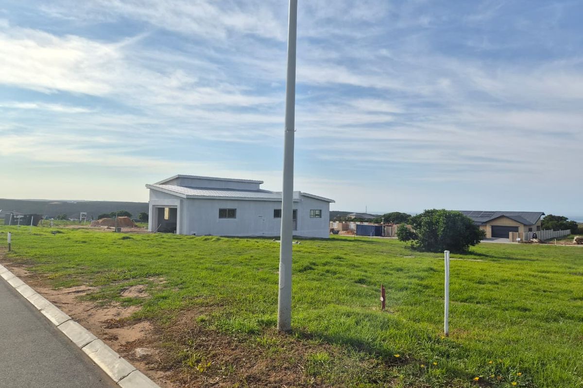 A view of a residential vacant land plot featuring a grassy landscape and a utility pole, with a neighboring structure visible in the background.