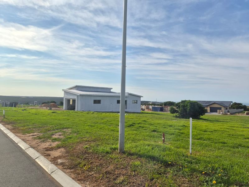 A view of a residential vacant land plot featuring a grassy landscape and a utility pole, with a neighboring structure visible in the background.