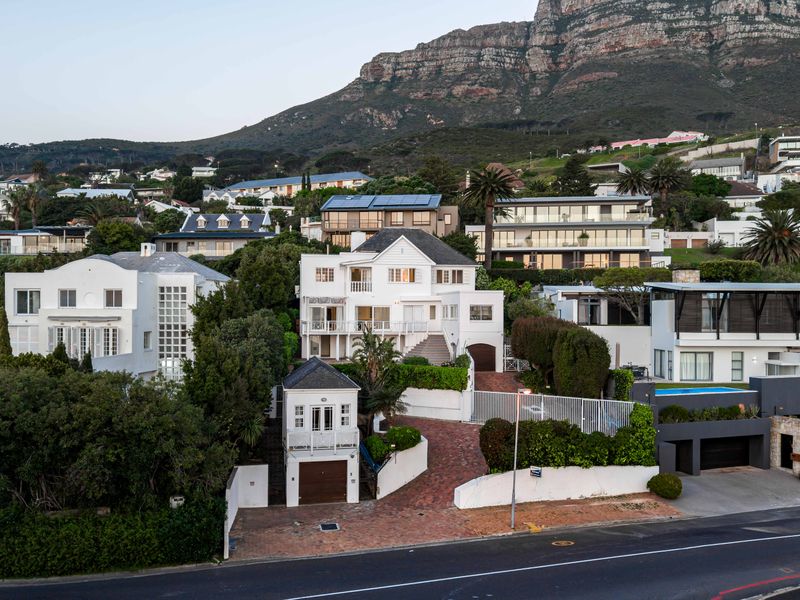 Aerial view of a multi-level residential property featuring a brick driveway, gated entrance, and landscaped garden set against a mountain backdrop.