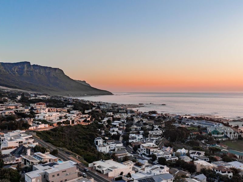 An elevated aerial view of a coastal residential neighborhood nestled between a mountain range and the ocean at sunset.
