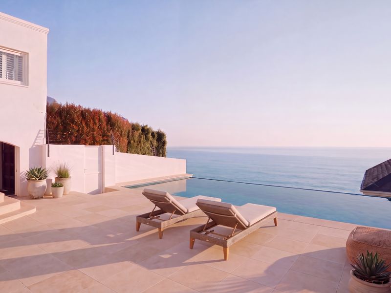 Stunning infinity edge pool area featuring stone paving, expansive ocean views, and direct access to the main residence's exterior.