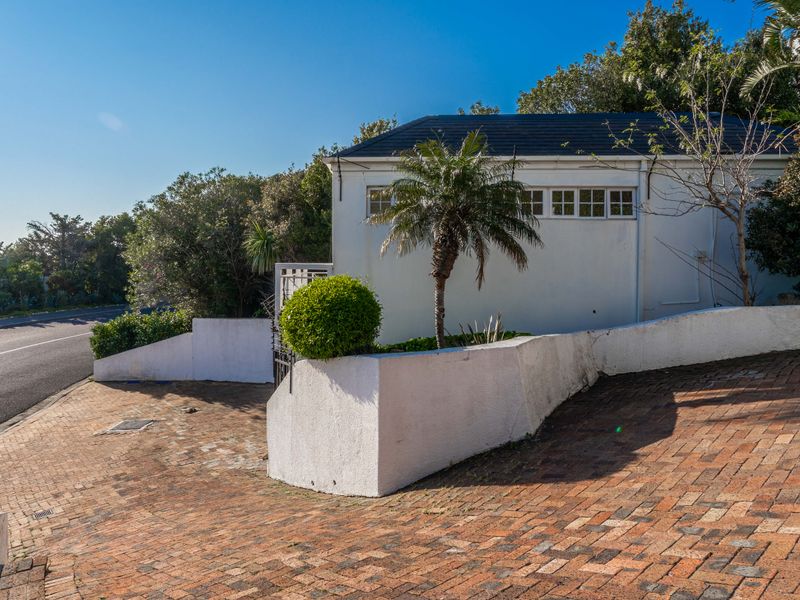 Front exterior view of the property featuring a brick paved driveway, white retaining walls, and a pitched roof structure.