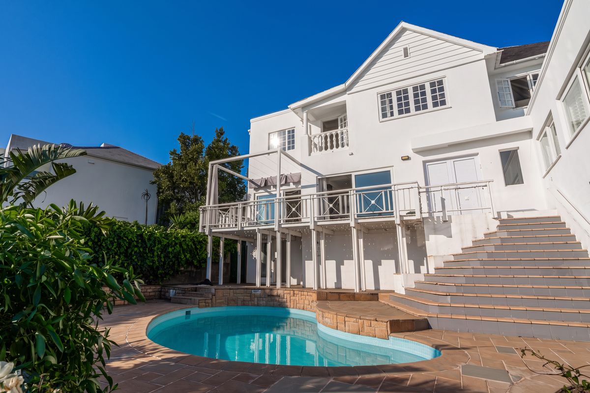 Rear view of the property featuring a swimming pool, raised wooden deck, and tiled staircase leading to the upper level.