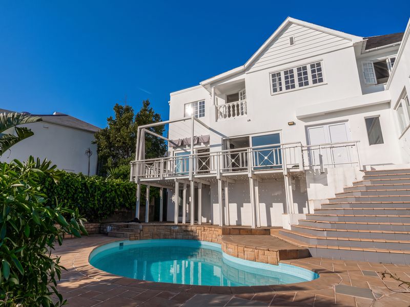 Rear view of the property featuring a swimming pool, raised wooden deck, and tiled staircase leading to the upper level.