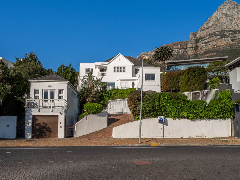 Front elevation of a multi-level residential property featuring a garage, paved driveway, and elevated balcony, set against a mountain backdrop.