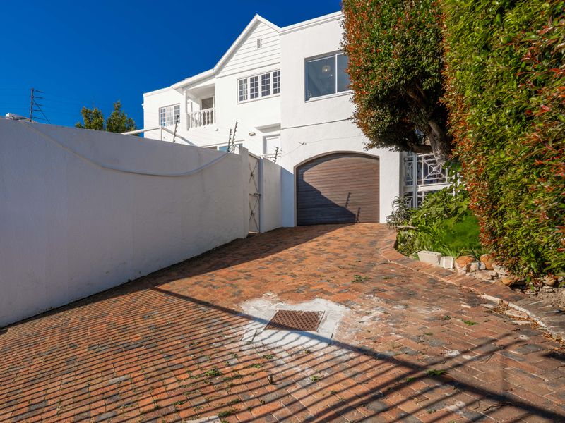 Front exterior view featuring a brick-paved driveway, secure boundary wall with electric fencing, and a single garage entrance.