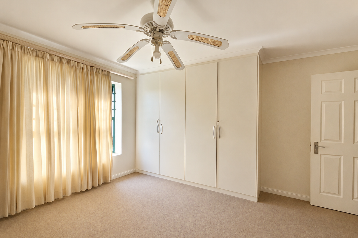 A bright, empty bedroom featuring neutral carpeting, built-in floor-to-ceiling cupboards, and a ceiling fan, offering a clean and versatile space.