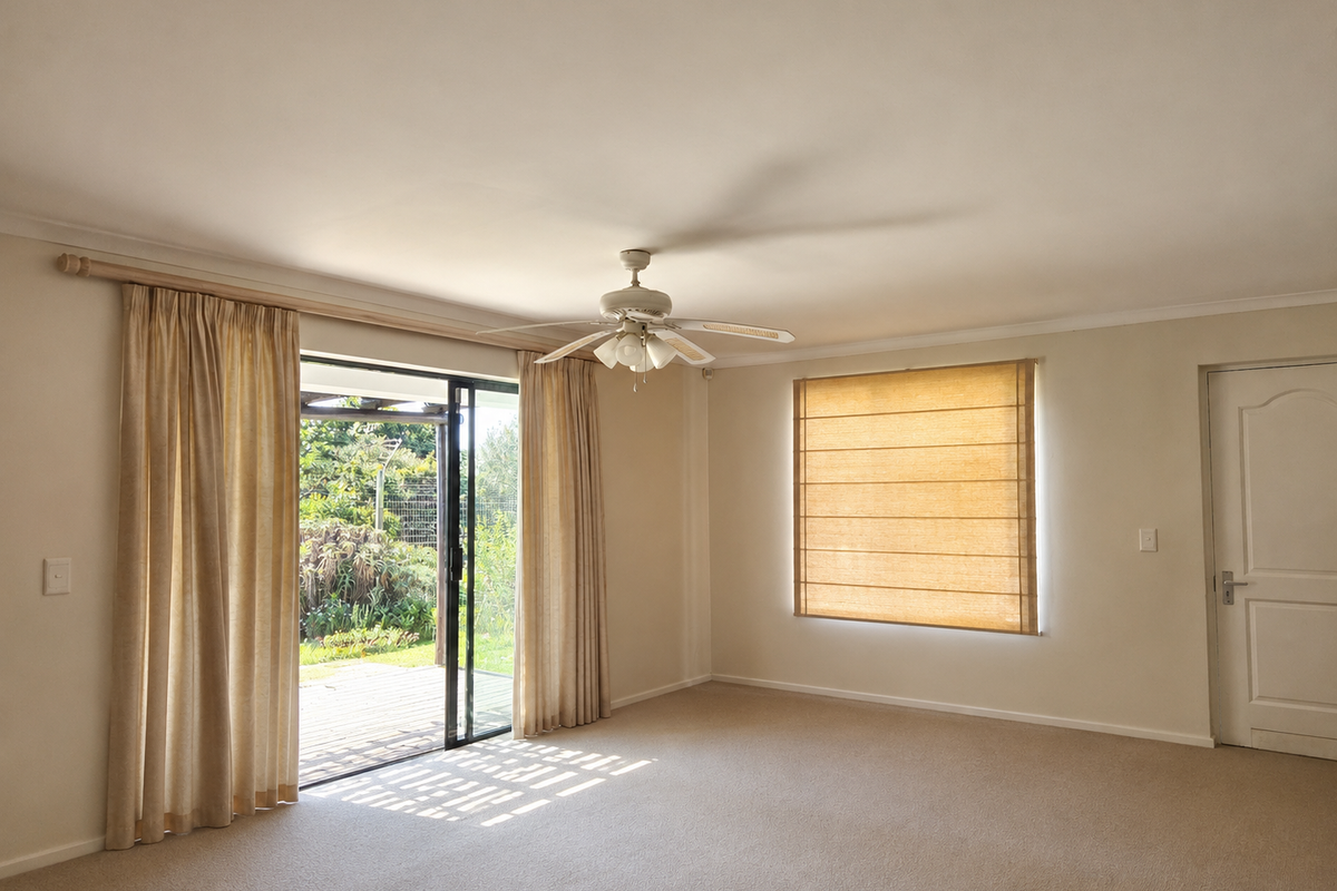 Spacious living room featuring neutral carpeting, a ceiling fan, and sliding glass doors providing direct access to the outdoor patio area.