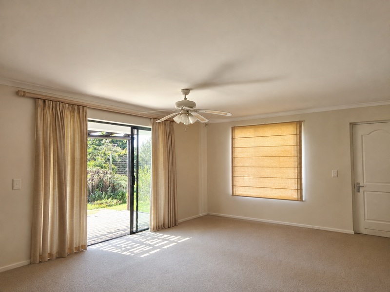Spacious living room featuring neutral carpeting, a ceiling fan, and sliding glass doors providing direct access to the outdoor patio area.