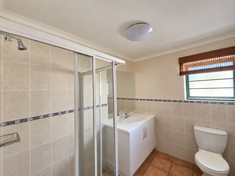 A clean, functional bathroom featuring a shower enclosure, vanity with basin, and toilet, finished with neutral wall tiles and terracotta floor tiles.