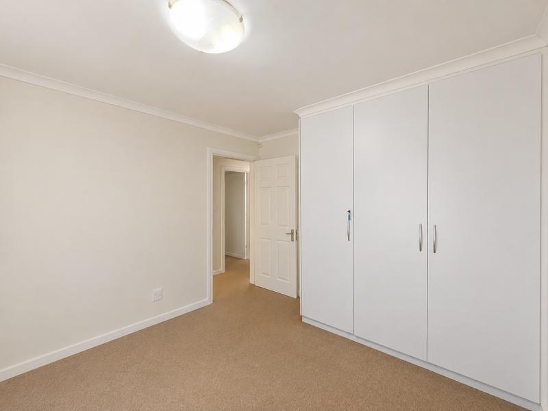 A clean, empty bedroom featuring neutral carpeting, built-in white cupboards, and coved cornicing, offering a bright and versatile living space.