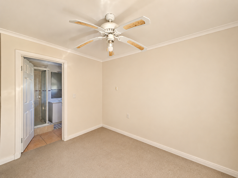 An empty bedroom featuring neutral carpeting, a ceiling fan, and direct access to an en-suite bathroom.