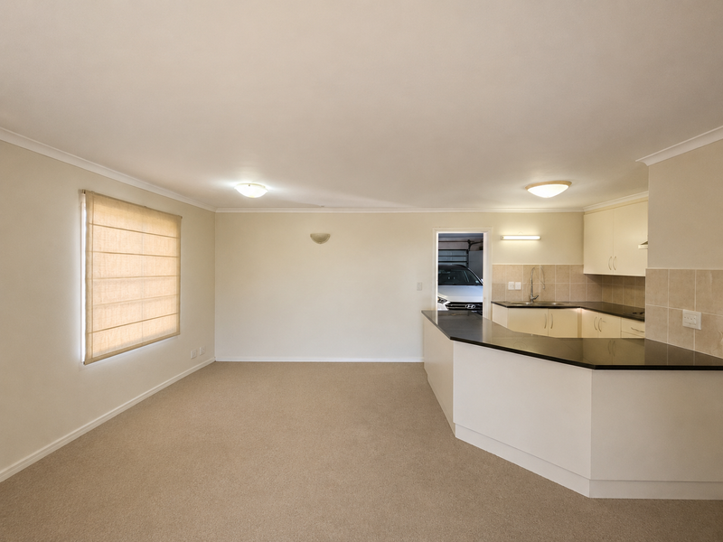 Spacious open-plan living area featuring a functional kitchen with granite countertops, neutral carpeting, and ample natural light from the side window.