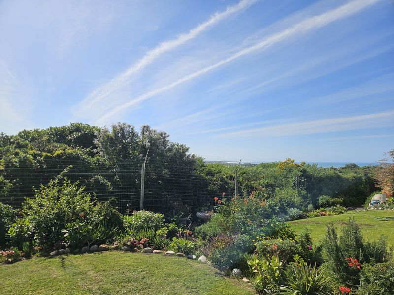 A well-maintained garden featuring lush greenery, a manicured lawn, and secure perimeter electric fencing with a distant coastal view.