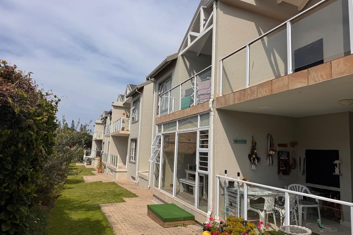 Rear view of a multi-story apartment complex featuring private balconies with glass balustrades, sliding doors, and a well-maintained communal garden area.