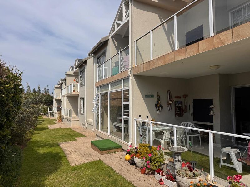 Rear view of the apartment complex featuring ground floor patios, upper-level balconies with glass balustrades, and a well-maintained communal lawn area.