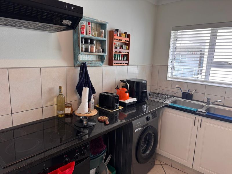 A functional kitchen featuring granite countertops, a built-in electric hob with extractor fan, double basin sink, and white cabinetry with tiled splashbacks.
