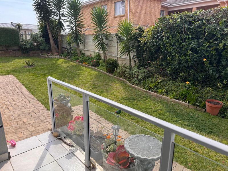 A tiled balcony featuring a modern glass balustrade overlooking a well-maintained private garden with paved pathways and established landscaping.