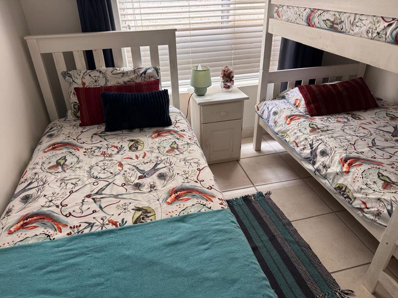 A functional bedroom featuring tiled flooring and venetian blinds, currently configured with bunk beds and a single bed.