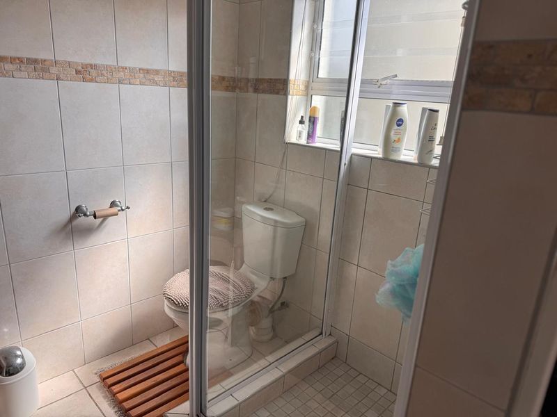 A functional bathroom featuring a glass-enclosed shower, a standard toilet, and neutral wall and floor tiling.