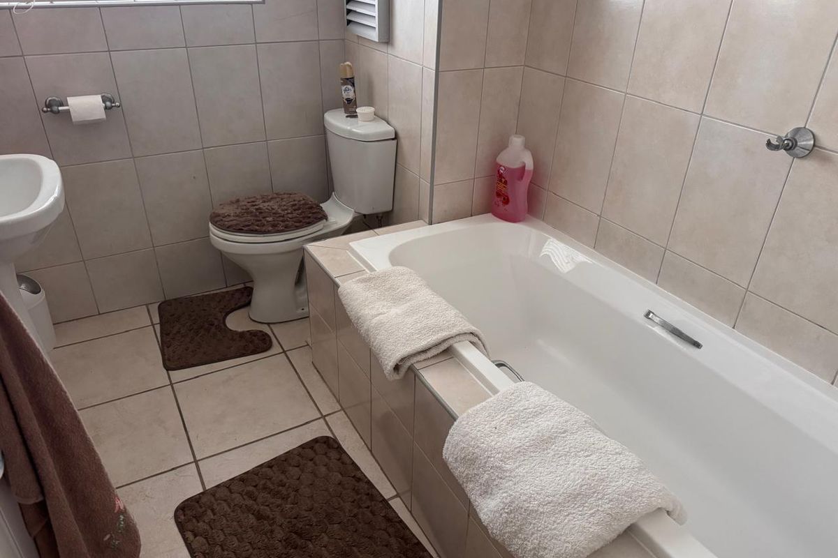 A functional bathroom featuring a built-in bathtub, pedestal basin, and neutral ceramic tiling throughout.