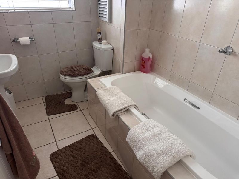 A functional bathroom featuring a built-in bathtub, pedestal basin, and neutral ceramic tiling throughout.