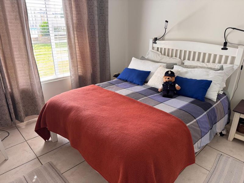 A functional bedroom featuring tiled flooring and large windows with venetian blinds, providing natural light and a view of the exterior.