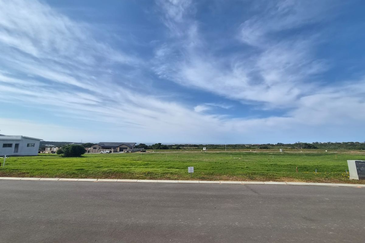 A wide-angle view of a vacant residential plot featuring a level grass surface, paved road frontage, and established utility connections.