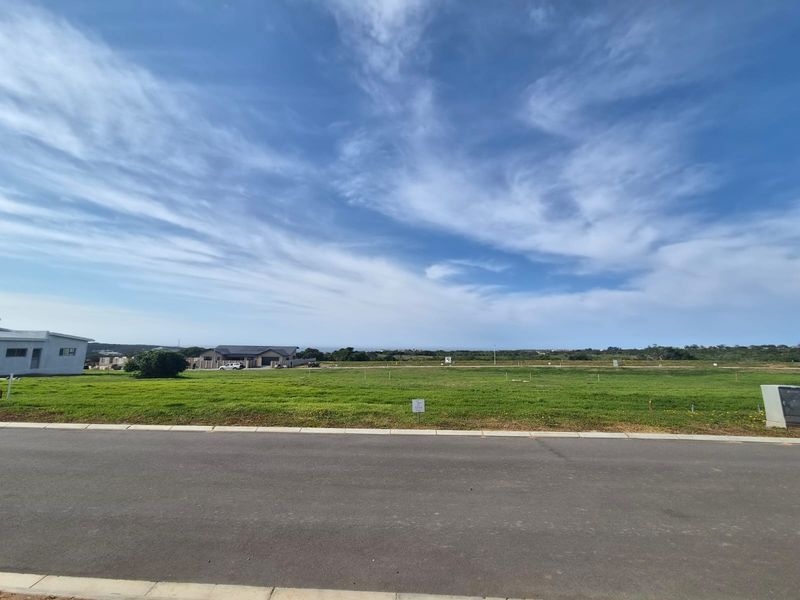 A wide-angle view of a vacant residential plot featuring a level grass surface, paved road frontage, and established utility connections.