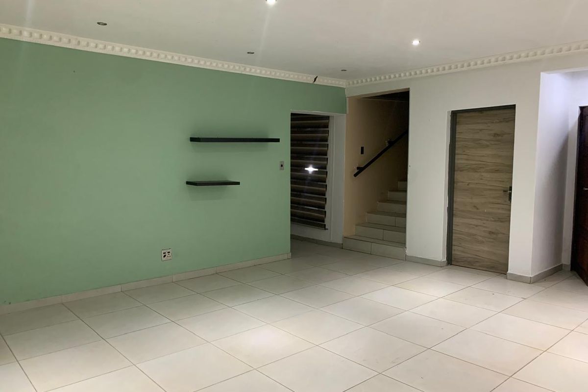 An empty living area featuring tiled floors, recessed lighting, crown molding, and a staircase leading to the upper level.