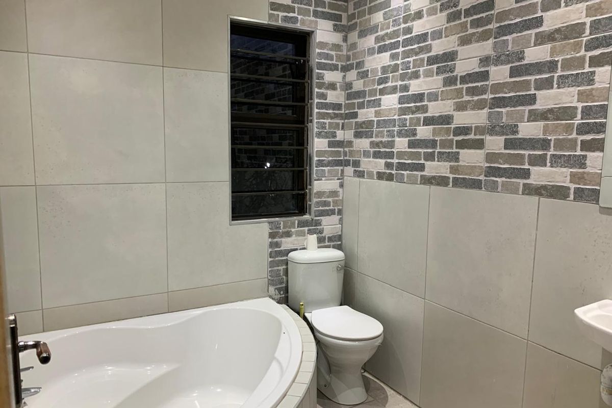 A modern bathroom featuring a corner bathtub, toilet, and wall-mounted basin with a mix of large format and decorative brick-style wall tiles.