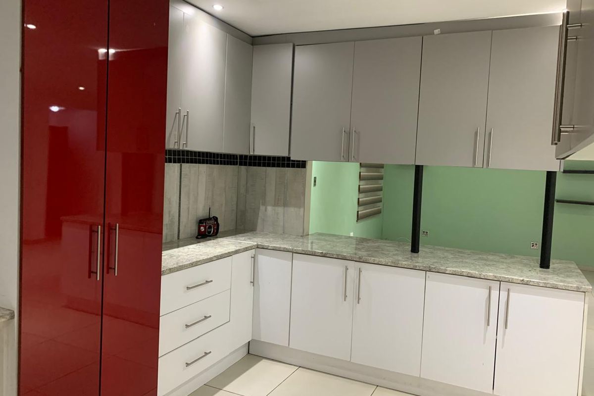 A modern kitchen featuring high-gloss red and white cabinetry, stone countertops, and tiled flooring, offering a clean and functional workspace.