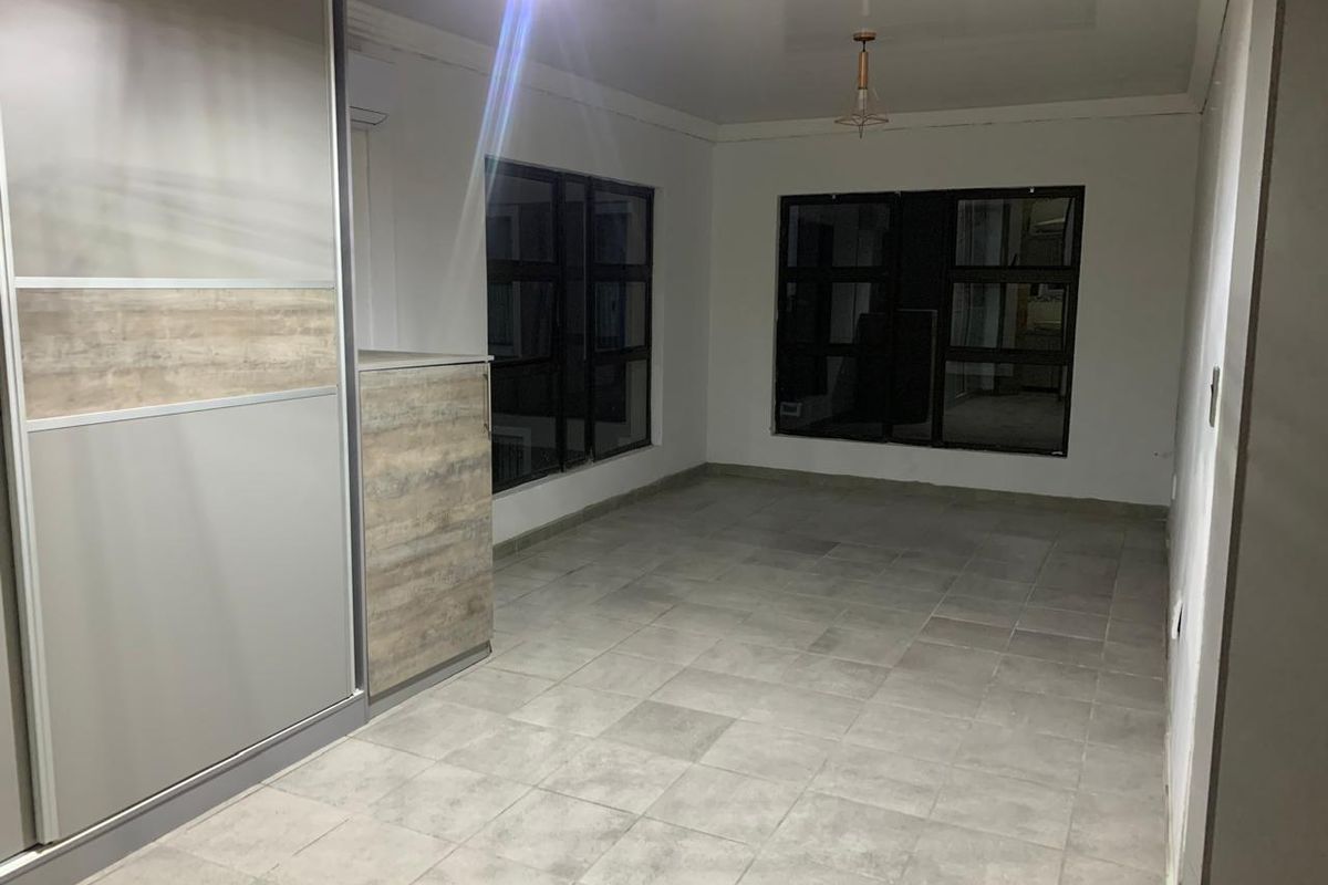 A clean, empty bedroom featuring modern tiled flooring, built-in wardrobe cabinetry, and large aluminium-framed windows providing ample natural light.