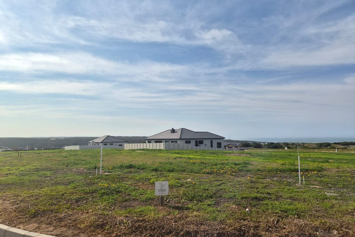 A vacant residential plot of land featuring clear boundary markers, situated in a developed estate with surrounding homes and distant coastal views.