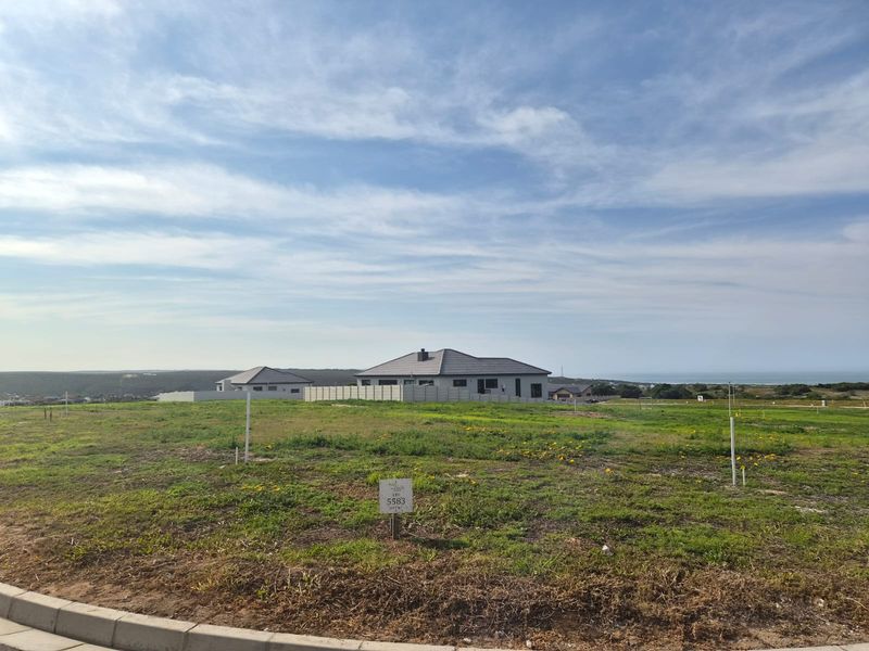 A vacant residential plot of land featuring clear boundary markers, situated in a developed estate with surrounding homes and distant coastal views.
